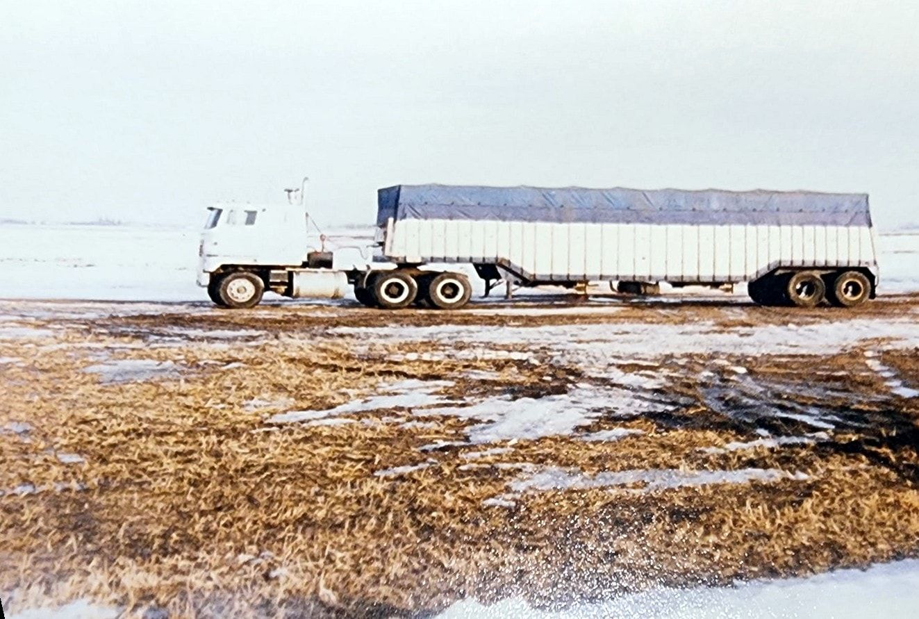 A white International cabover pulling a tarped hopper-bottom trailer across a snowy field.