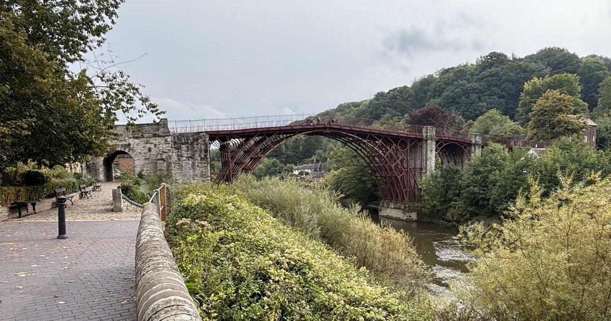 The Iron Bridge in Shropshire, painted red-brown, arching over the River Severn, seen from the riverside path
